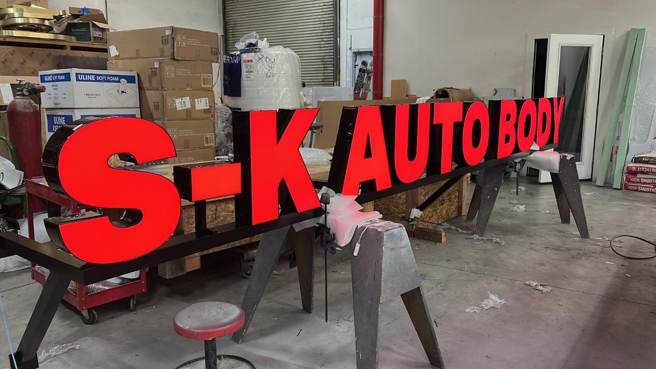 Large red front-illuminated S-K AUTO BODY channel letter sign resting on sawhorses during fabrication