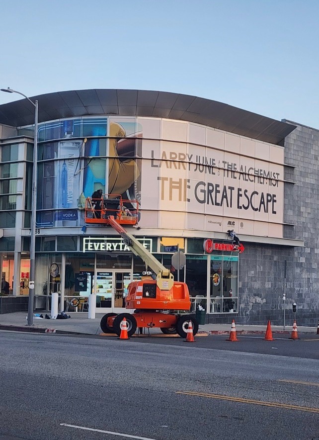 Large-format building wrap for Larry June and The Alchemist's The Great Escape on a curved Los Angeles storefront